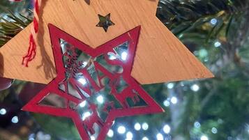 Un ornamento a forma di stella di legno con un'apertura a stella rossa, legato con un cordoncino rosso e bianco, appeso a un albero di Natale addobbato con luci.