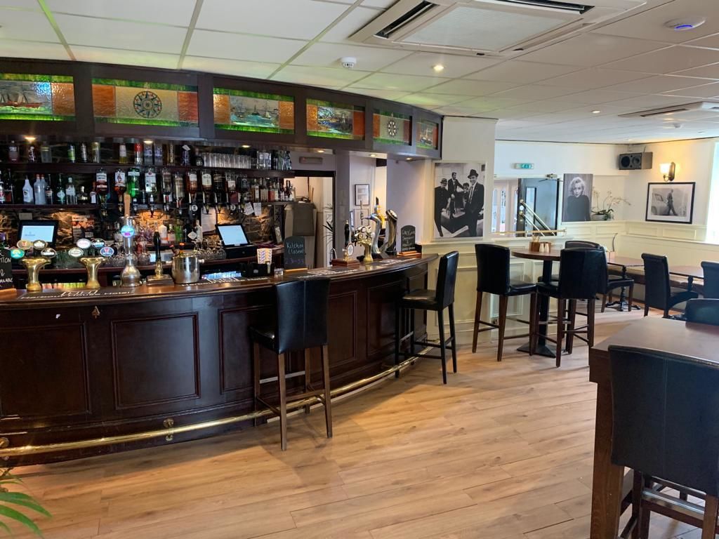 A bar area with a wooden counter, bar stools, and a seating area with tables and chairs.
