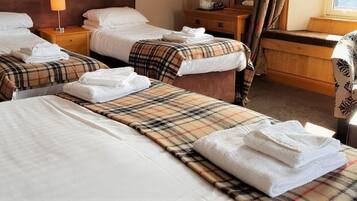 Habitació d'hotel amb dos llits, cadascun amb llençol de vellesa i tovallola doblegada. Hi ha una panxa de fusta i una cadira amb motius florals.