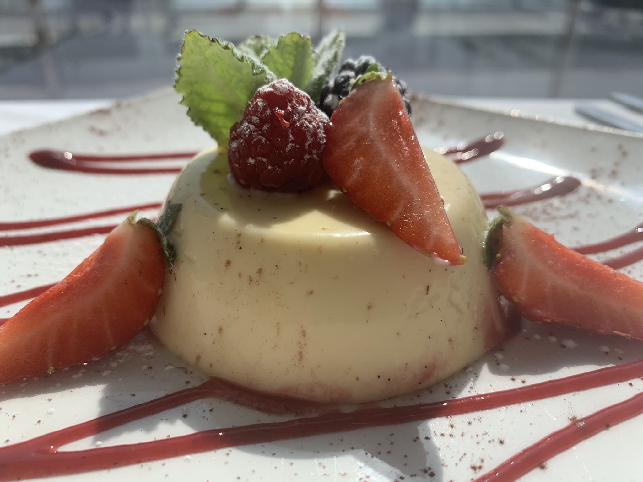 A dessert with strawberries and a berry on top, surrounded by chocolate sauce.