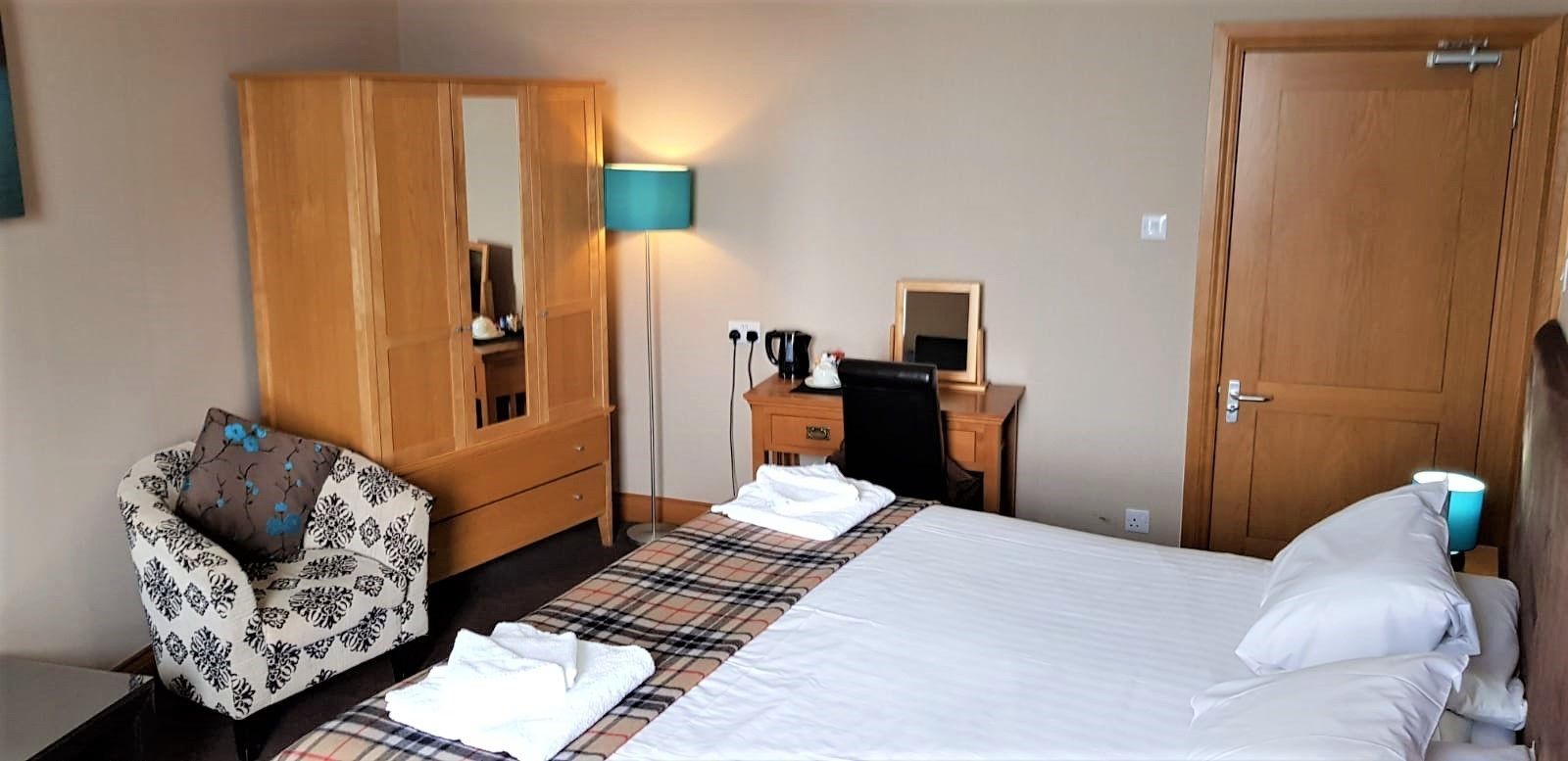 Une chambre d’hôtel comprenant un lit, une armoire, un bureau avec une chaise, une lampe et une petite table avec un miroir.