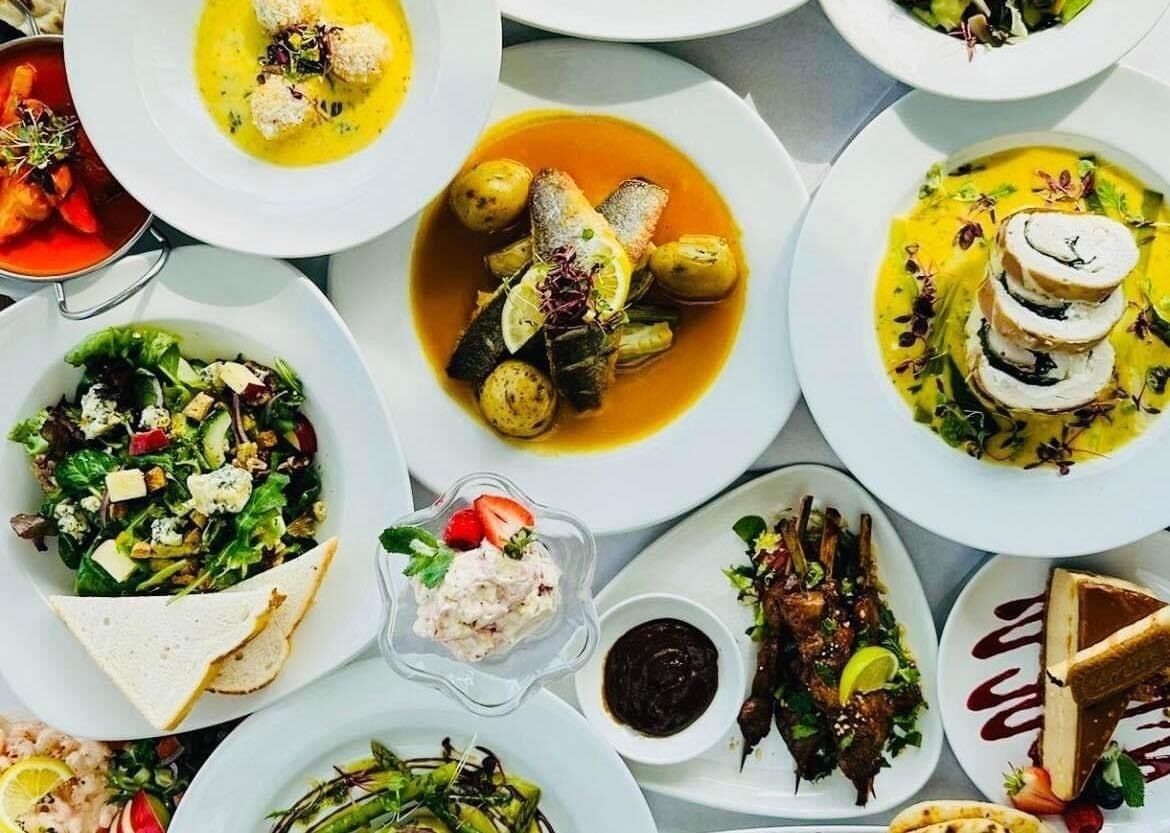 Diversos pratos em chapas brancas, incluindo mariscos, vegetais e uma sobremesa.