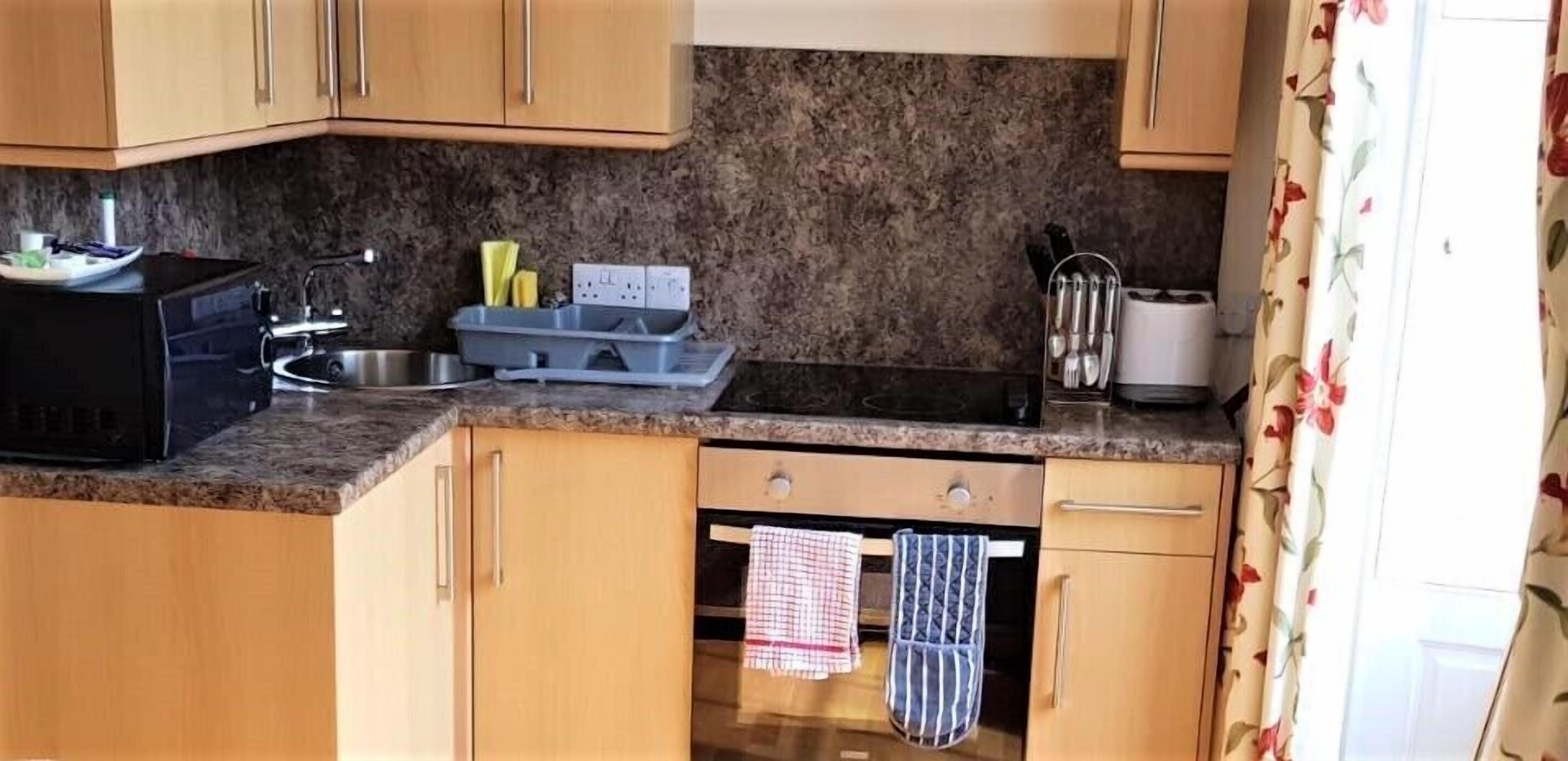Cucina con mobili in legno, piano di lavoro in granito, forno a microonde, lavello e scolapiatti.