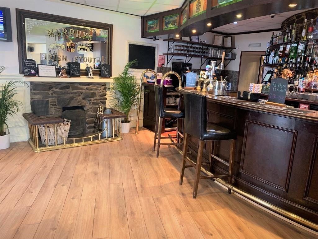 Un espace bar doté d’une cheminée en pierre, de tabourets et de diverses bouteilles exposées sur des étagères.