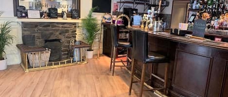 Un espace bar doté d’une cheminée en pierre, de tabourets et de diverses bouteilles exposées sur des étagères.