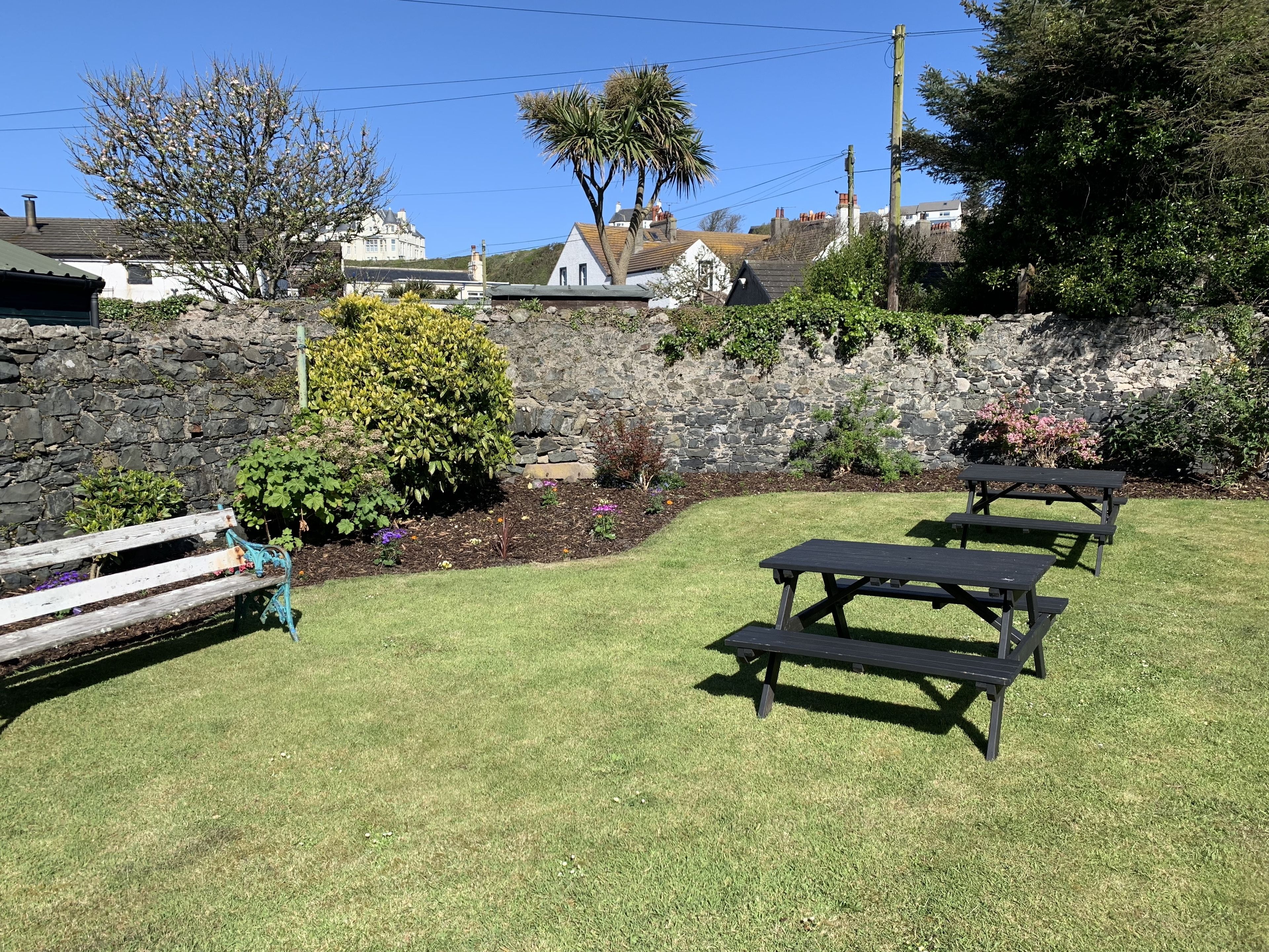 A grassy outdoor area with stone walls, a wooden bench, and picnic tables.