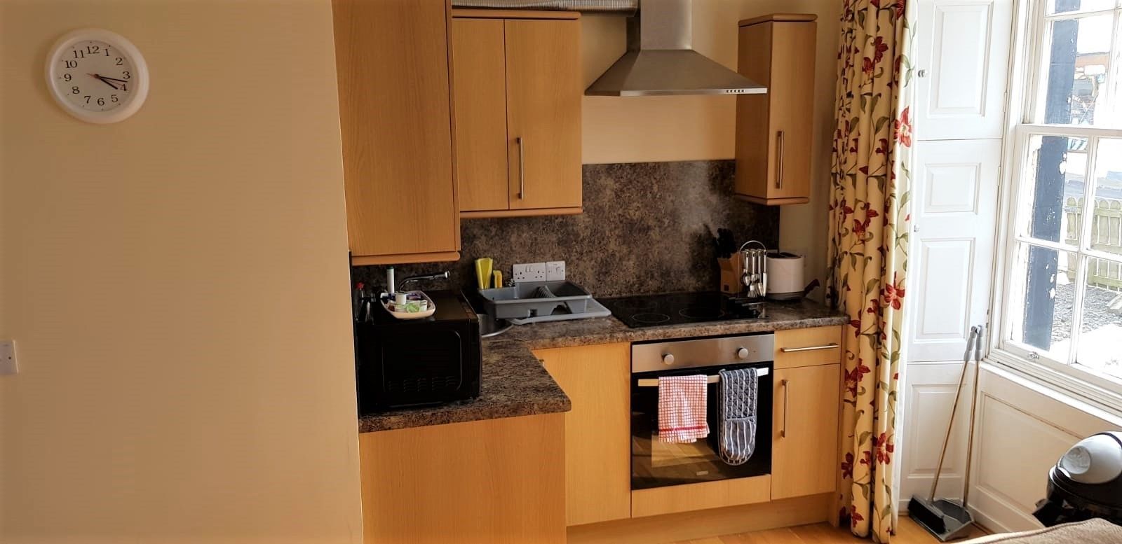 A compact kitchen with wooden cabinets, a stove, oven, and a clock on the wall.