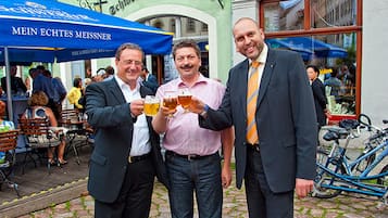 Three men holding glasses of beer in front of a building with a sign that reads "Hotel Zum Wassert G."