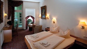 A hotel room with two beds, a desk, a chair, a small table, and a balcony with a view.