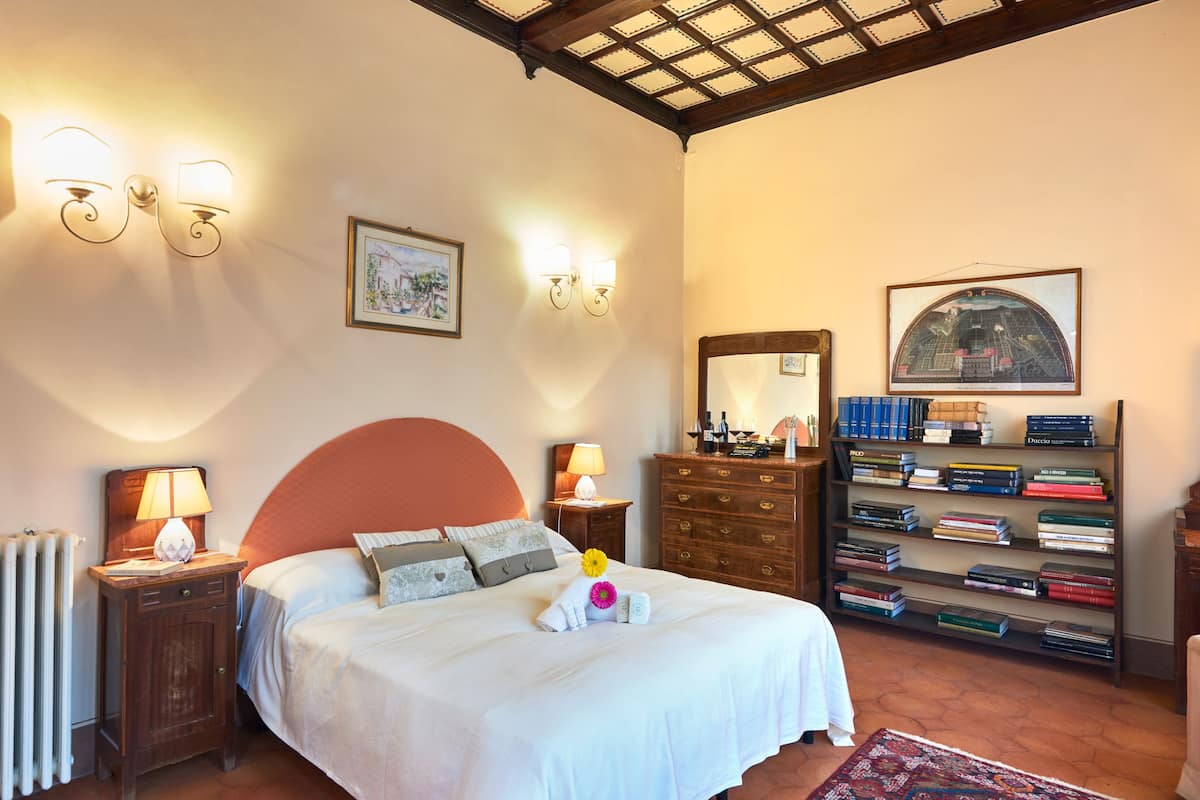 A bedroom with a bed, bedside lamps, a dresser, a bookshelf, and a radiator.