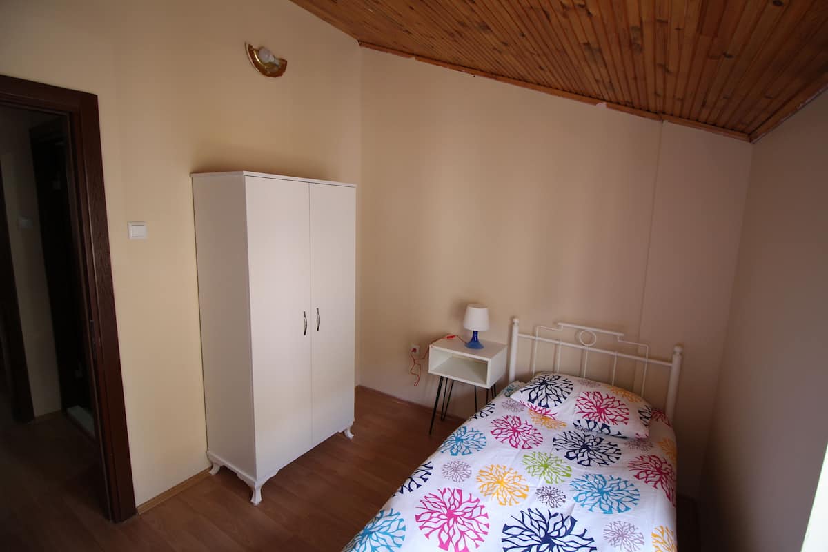 A bedroom with a bed, a wardrobe, a small table with a lamp, and a wooden ceiling.