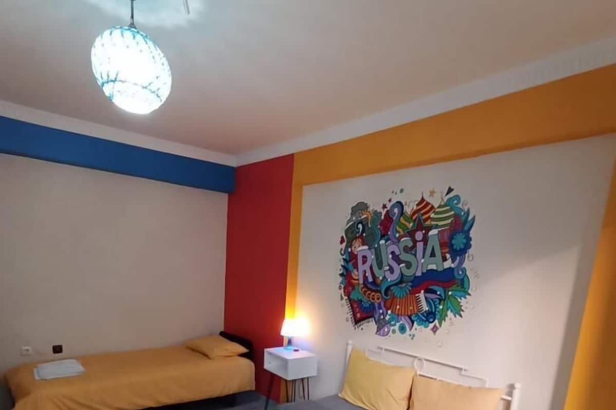 A hotel room with two single beds, a large bed, a wall decoration, and a ceiling light.