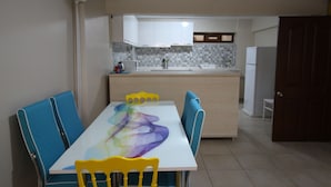 A dining area with a table and chairs, a kitchen in the background, and a door to the right. - Deeps Hostel (Eskisehir)