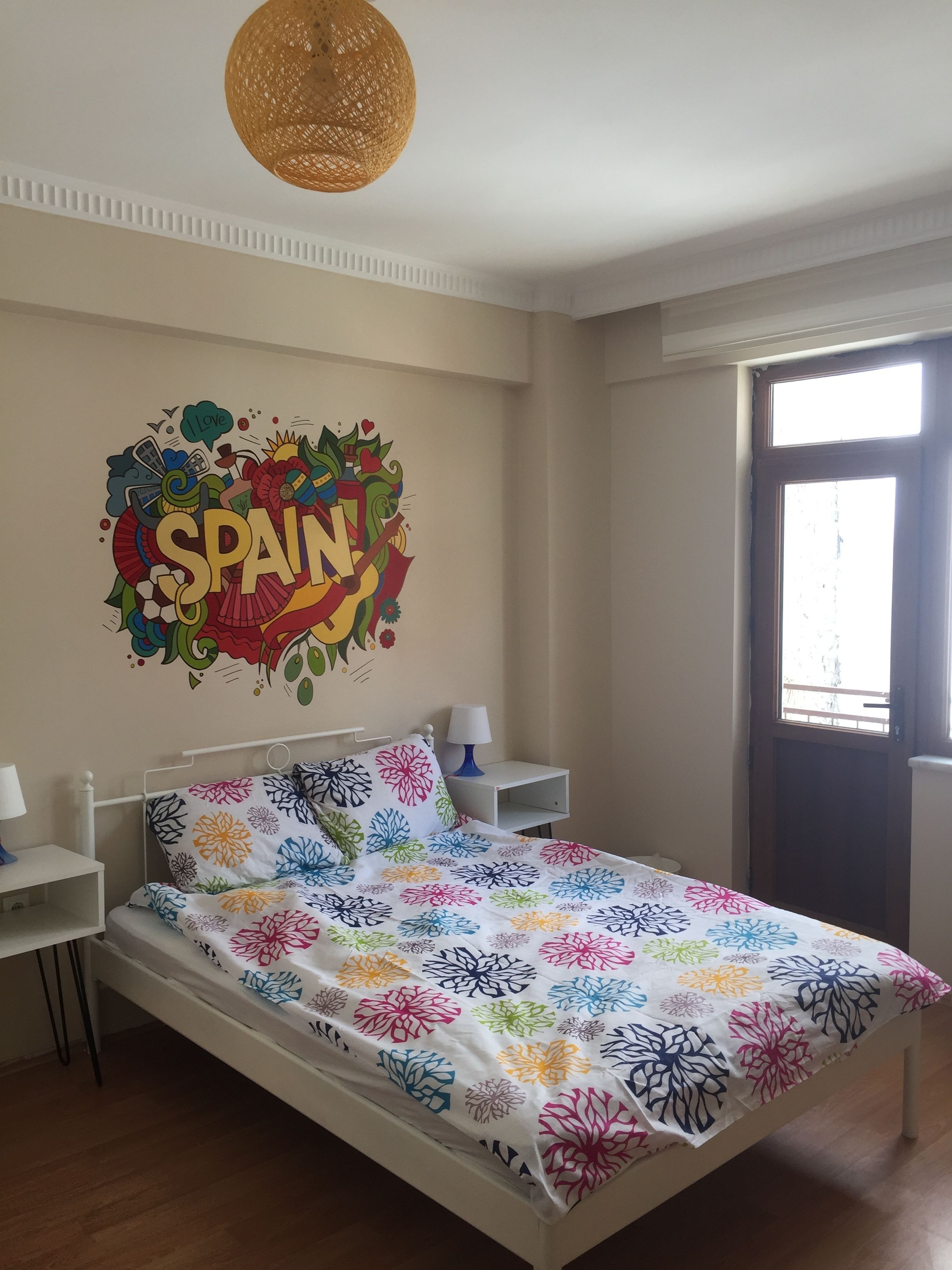 Un dormitorio con una cama, dos mesitas de noche, una decoración en la pared y una ventana.