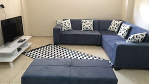 A modern living room with a sectional sofa, ottoman, and a flat-screen TV on a white stand. - Deeps Hostel (Eskisehir)