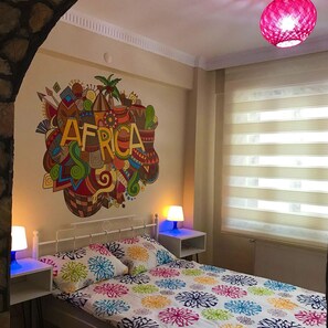 A bedroom with a bed, two bedside tables with lamps, a wall mural with 'AFRICA' written on it, and a window with blinds. - Deeps Hostel (Eskisehir)