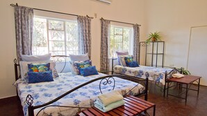 Quarto com duas camas, cada uma com colcha florida, um banco de madeira e uma mesinha.