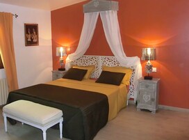 Quarto com cama, mesas de cabeceira, um banco e um dossel.