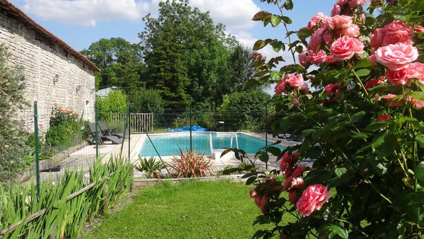 A swimming pool surrounded by a grassy area, a stone building, and blooming pink roses.