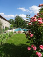 Piscina rodeada por um gramado, um edifício de pedra e rosas cor-de-rosa em flor.
