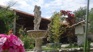A garden with a stone fountain, a statue, and a building with a tiled roof.