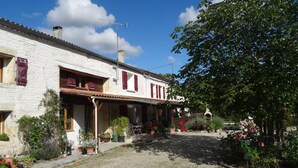 A traditional white building with red shutters, a cobblestone driveway, and a garden with potted plants and flowers.