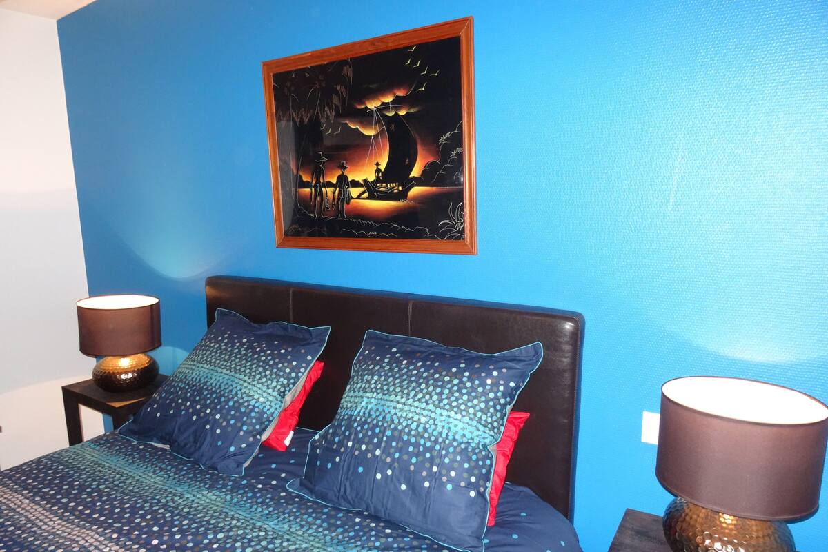 Ein Schlafzimmer mit einem Bett, zwei Kissen, einem Nachttisch mit Lampe und einem Bild an der Wand.