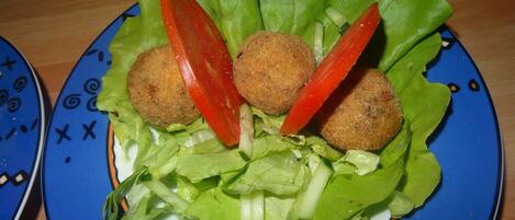 Un plato con tres preparaciones redondas, empanizadas, sobre hojas de lechuga, acompañado de rodajas de tomate.
