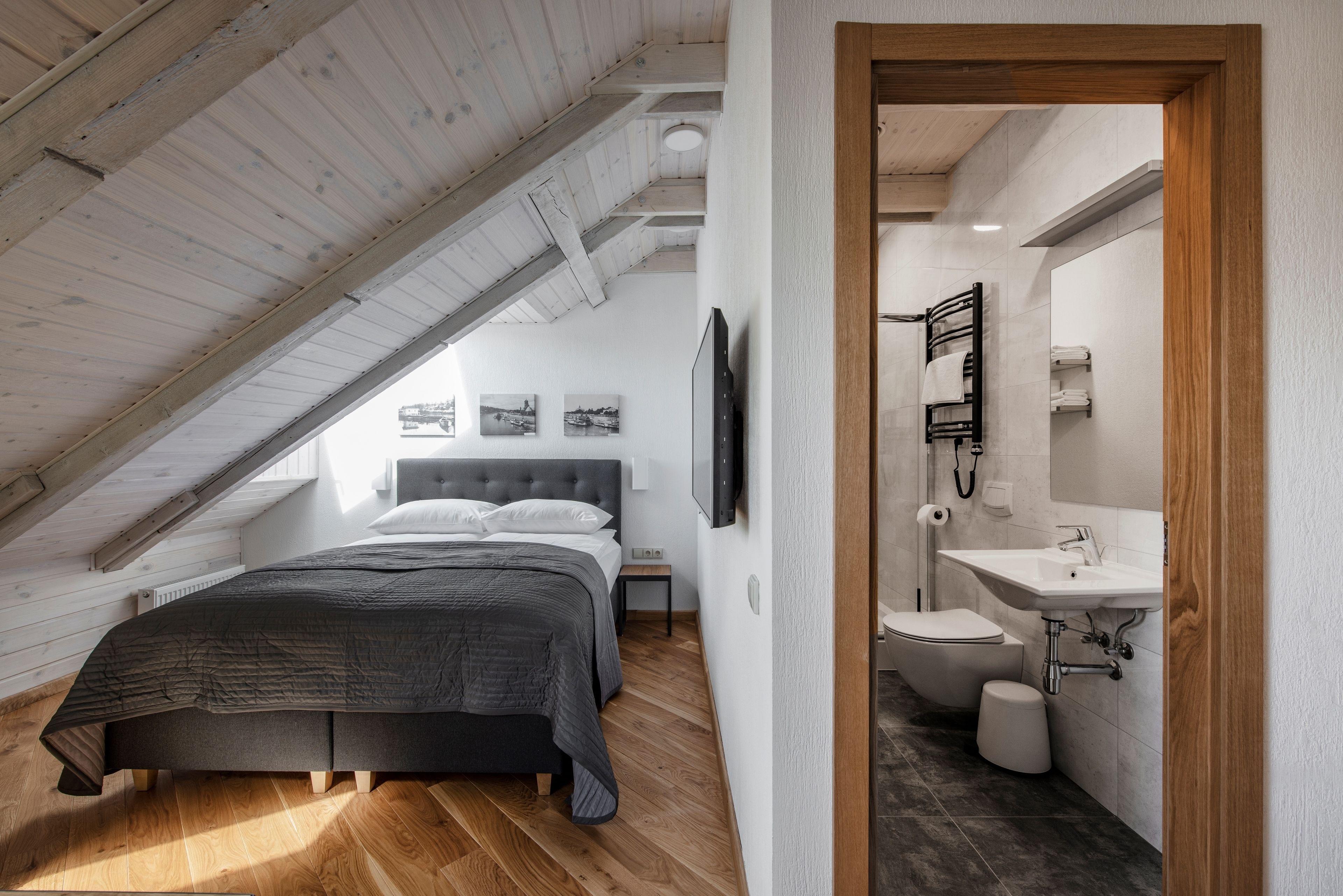 Een slaapkamer met een schuine kap, een bed, een televisie en een badkamer met een wastafel en toilet.
