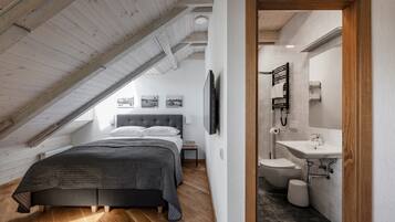 Een slaapkamer met een schuine kap, een bed, een televisie en een badkamer met een wastafel en toilet.