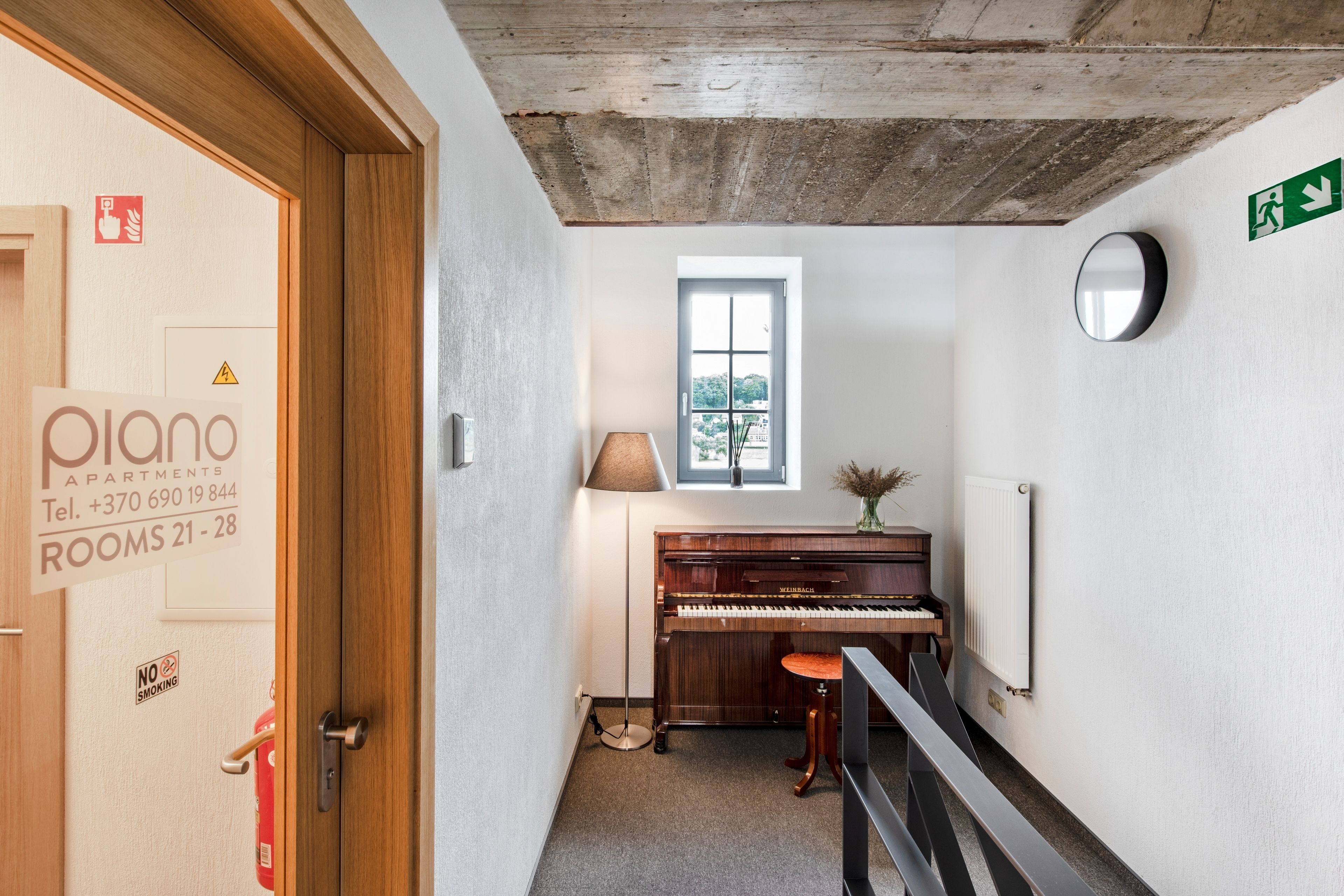 Un piano en un pasillo con una ventana, una lámpara y un extintor.