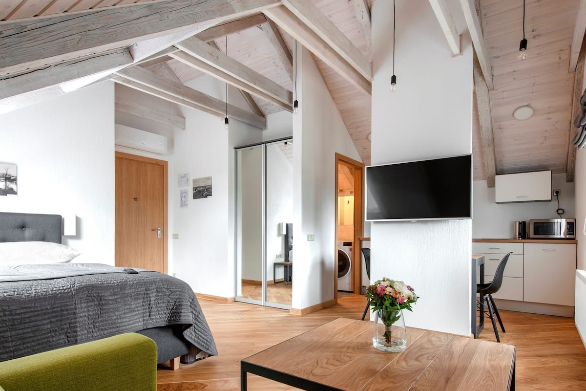 A modern, open-plan living space with a wooden ceiling, a flat-screen TV, a dining area, and a kitchen.