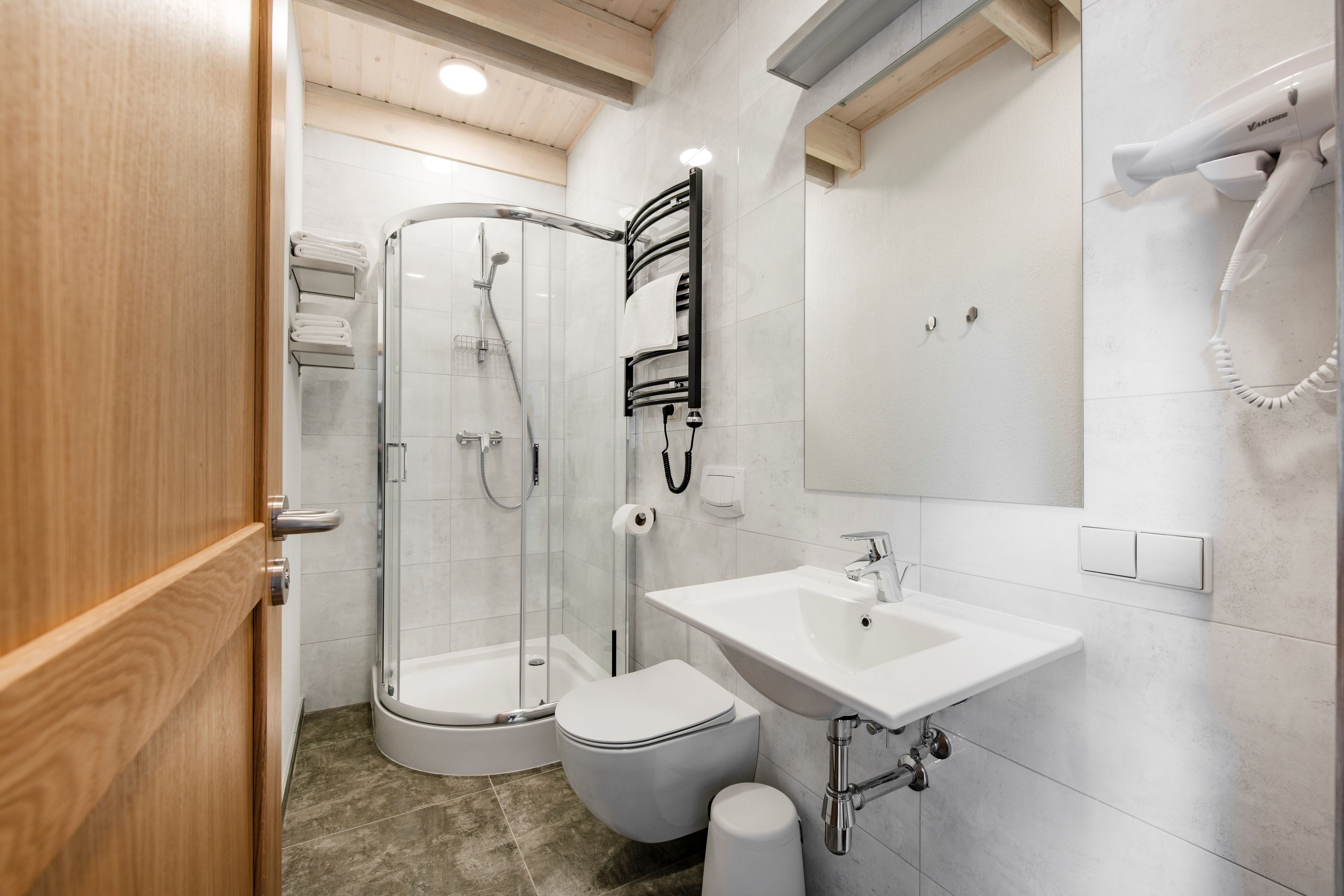 Et moderne badeværelse med en glasbrusekabine, en hvid vask og et toilet.