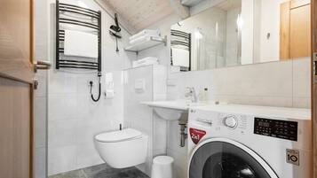 A compact bathroom with a washing machine, toilet, sink, and towel rack.
