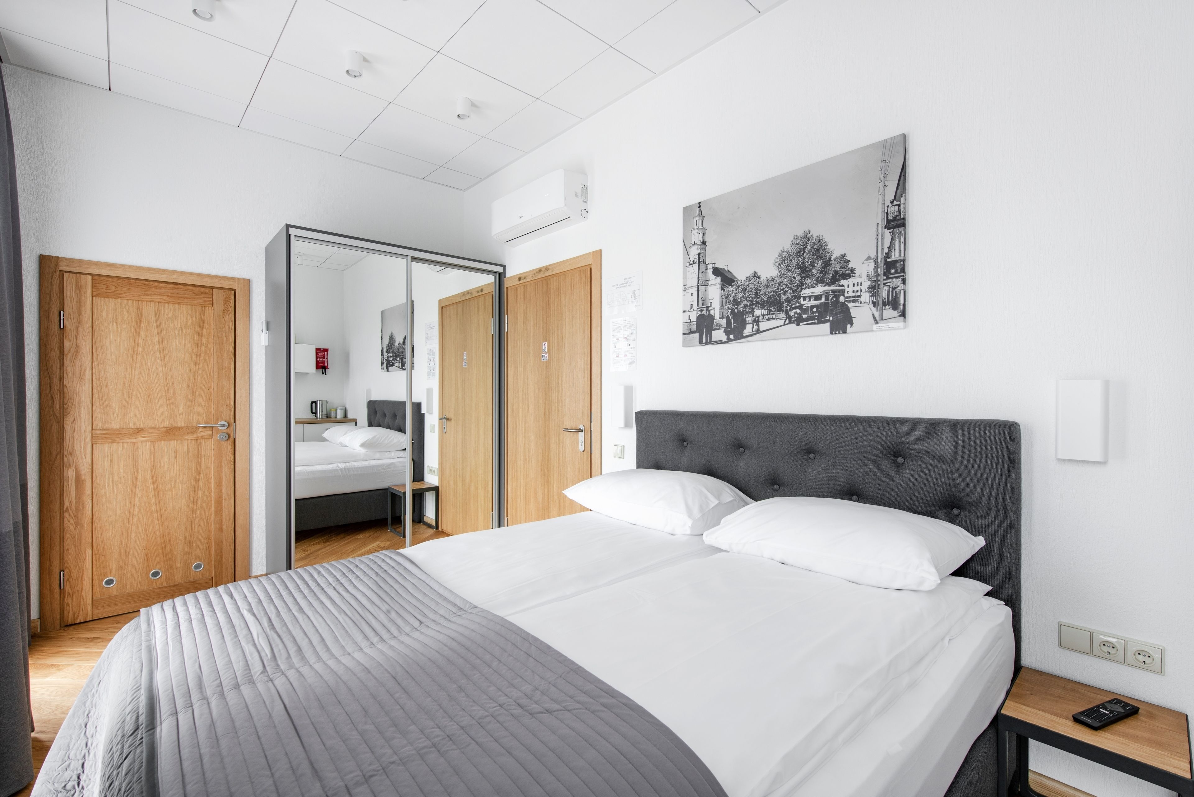 Una habitación de hotel moderna con una cama grande, un armario, un espejo y un cuadro colgado en la pared.
