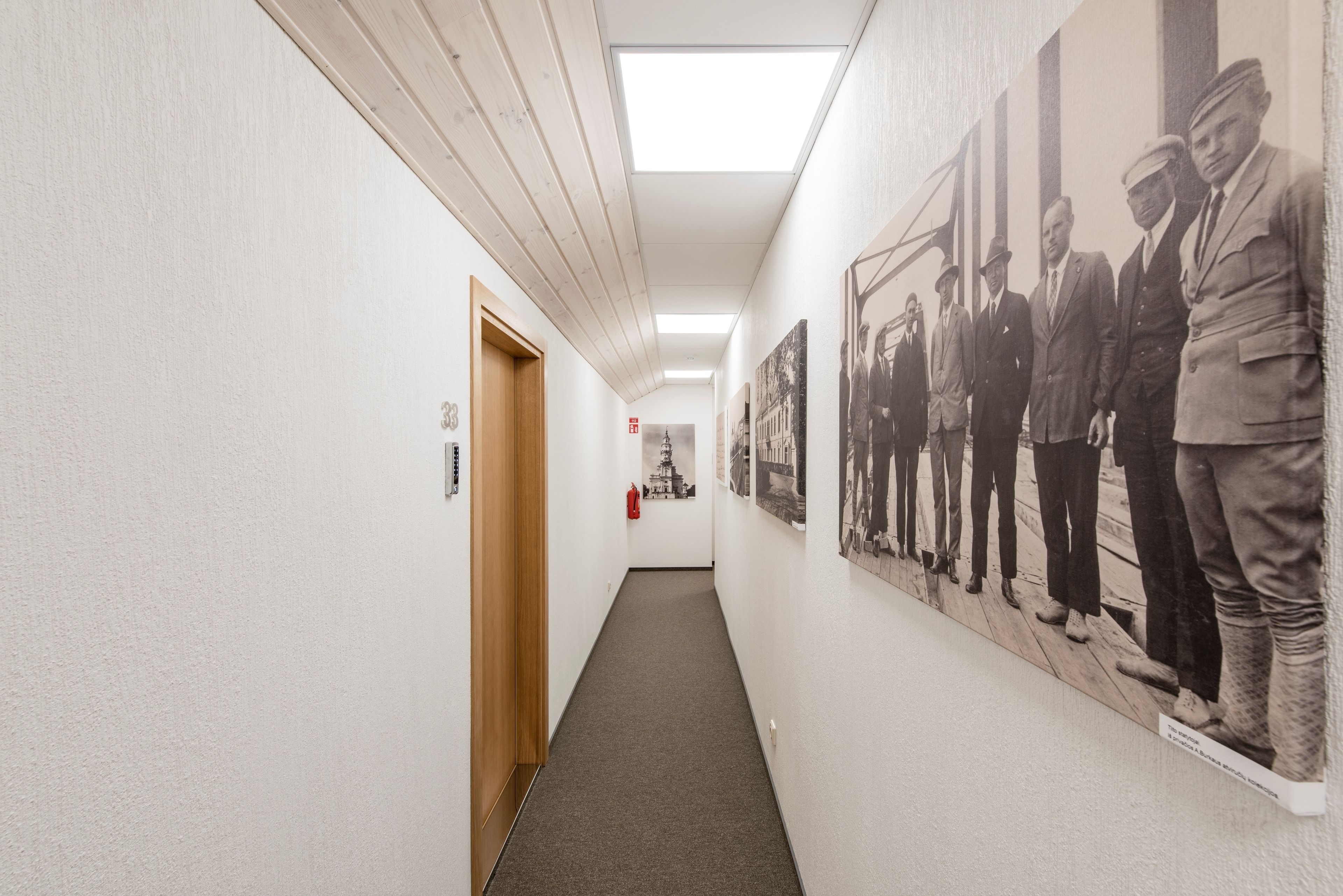 A hallway with a wooden door, a fire extinguisher, and a black and white photograph on the wall.
