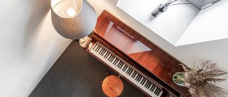 A piano, a lamp, and a vase with dried flowers on a table in a room with a window and a plant.