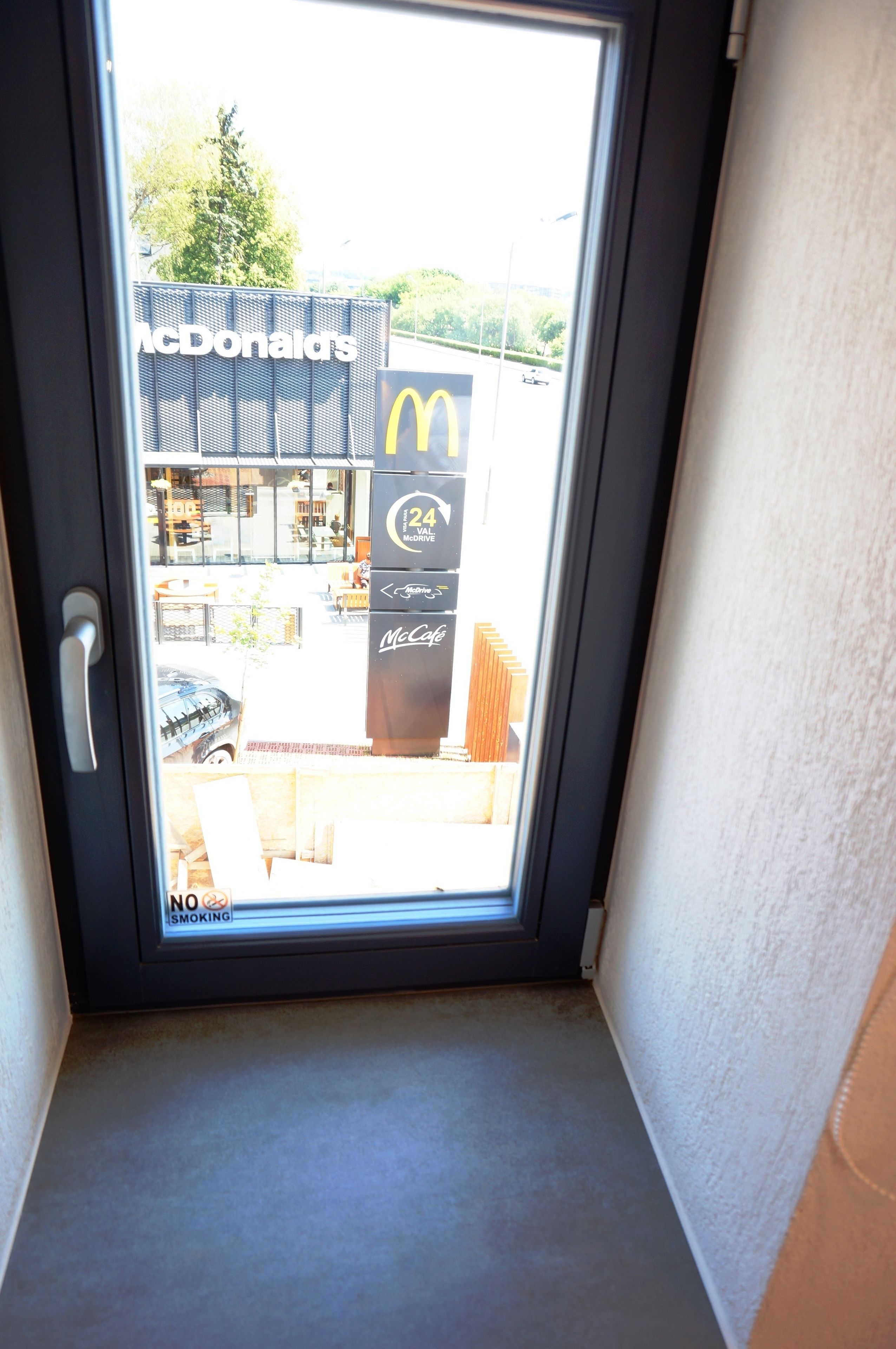 Vista a través de una ventana de un restaurante McDonald's, con un letrero que indica '24 horas Drive-Thru' y un letrero de 'No Fumar'.
