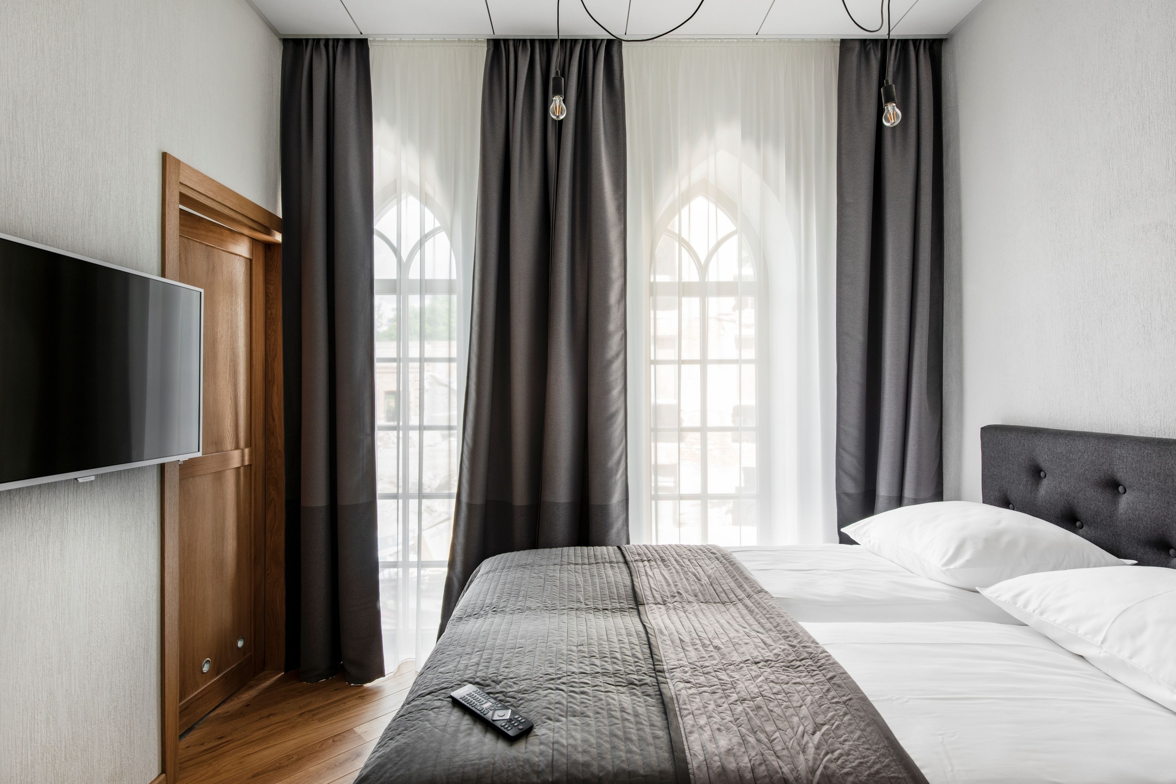 A modern hotel room with a large bed, a flat-screen TV, and a wooden wardrobe.