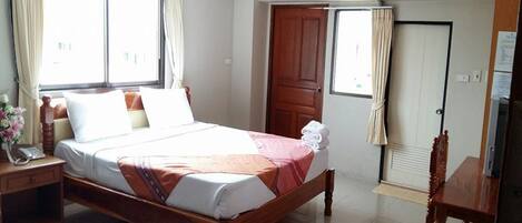 Habitación de hotel con cama de madera, escritorio, silla, armario y aire acondicionado.