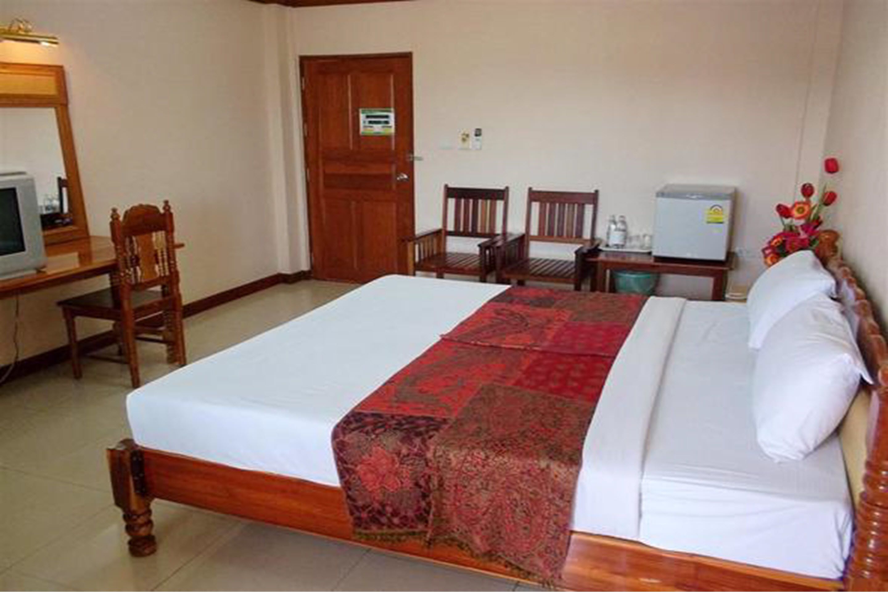 A hotel room with a large bed, a desk with a computer, a chair, and a small refrigerator.