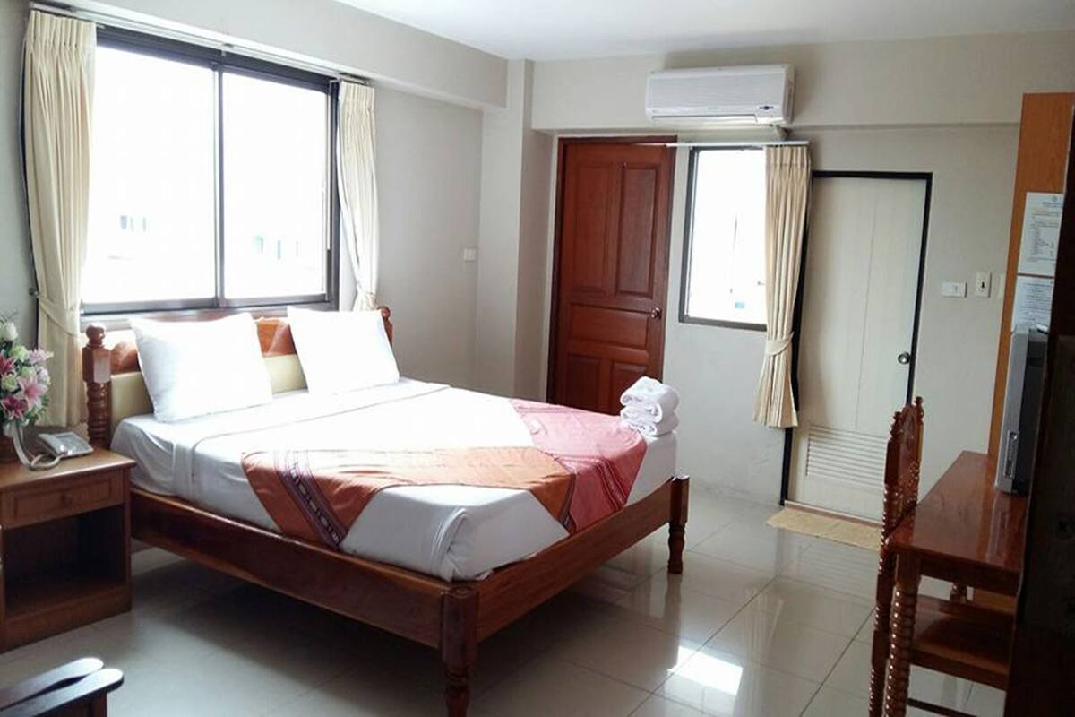 A hotel room with a bed, a desk, a chair, an air conditioning unit, and a door.