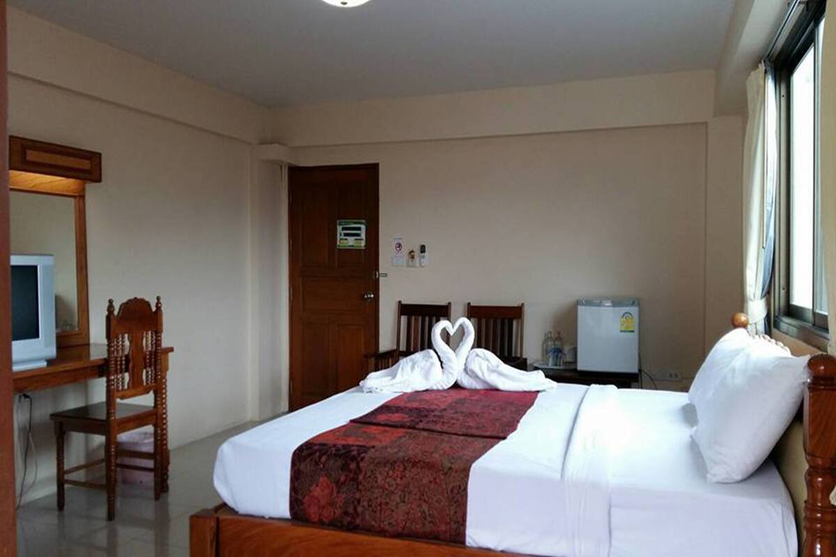 A hotel room with a bed, a desk, a chair, a television, and a refrigerator.
