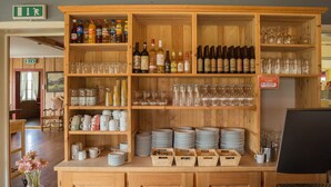 A wooden bar area with shelves of bottles, glasses, and plates.