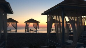 A beach with three beach umbrellas and lounge chairs.