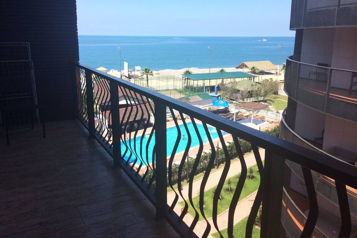 A balcony with a view of a swimming pool, a beach, and the ocean.