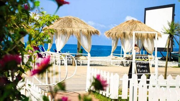 A beachside restaurant with thatched umbrellas and a white picket fence.
