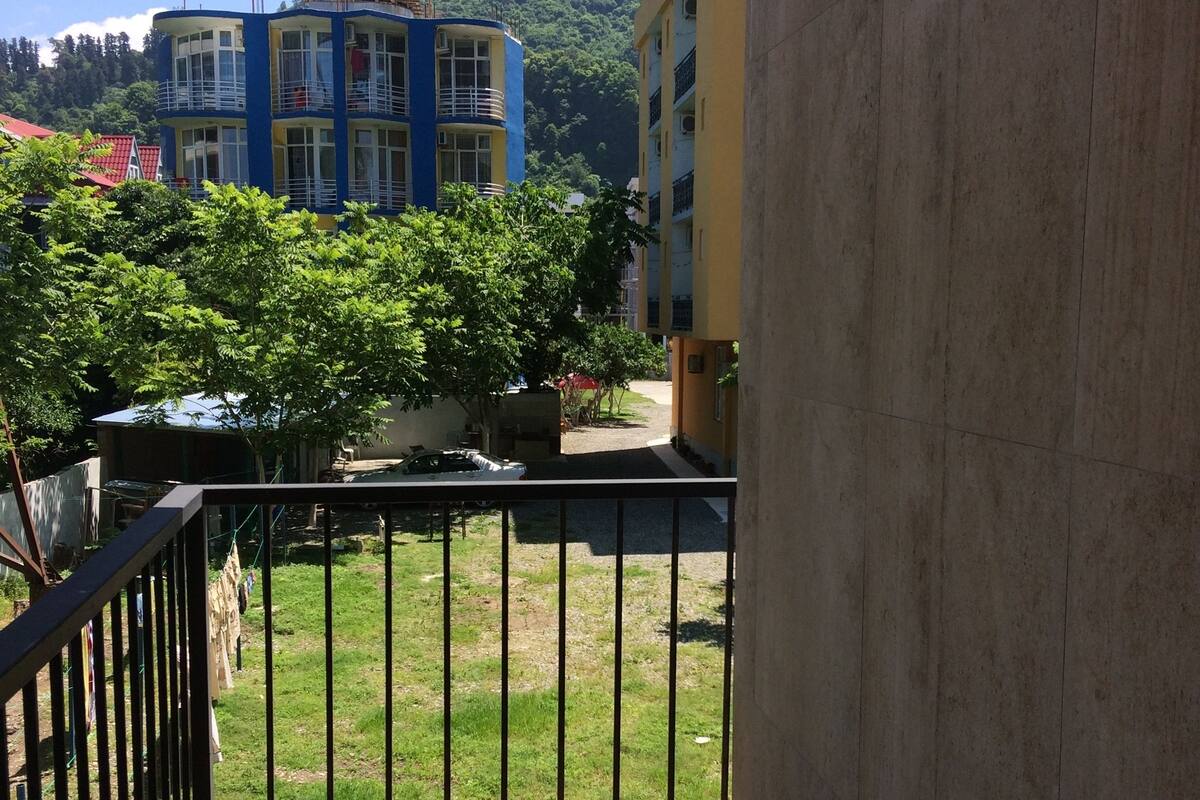 A balcony with a view of a building complex, a grassy area, and a tree.