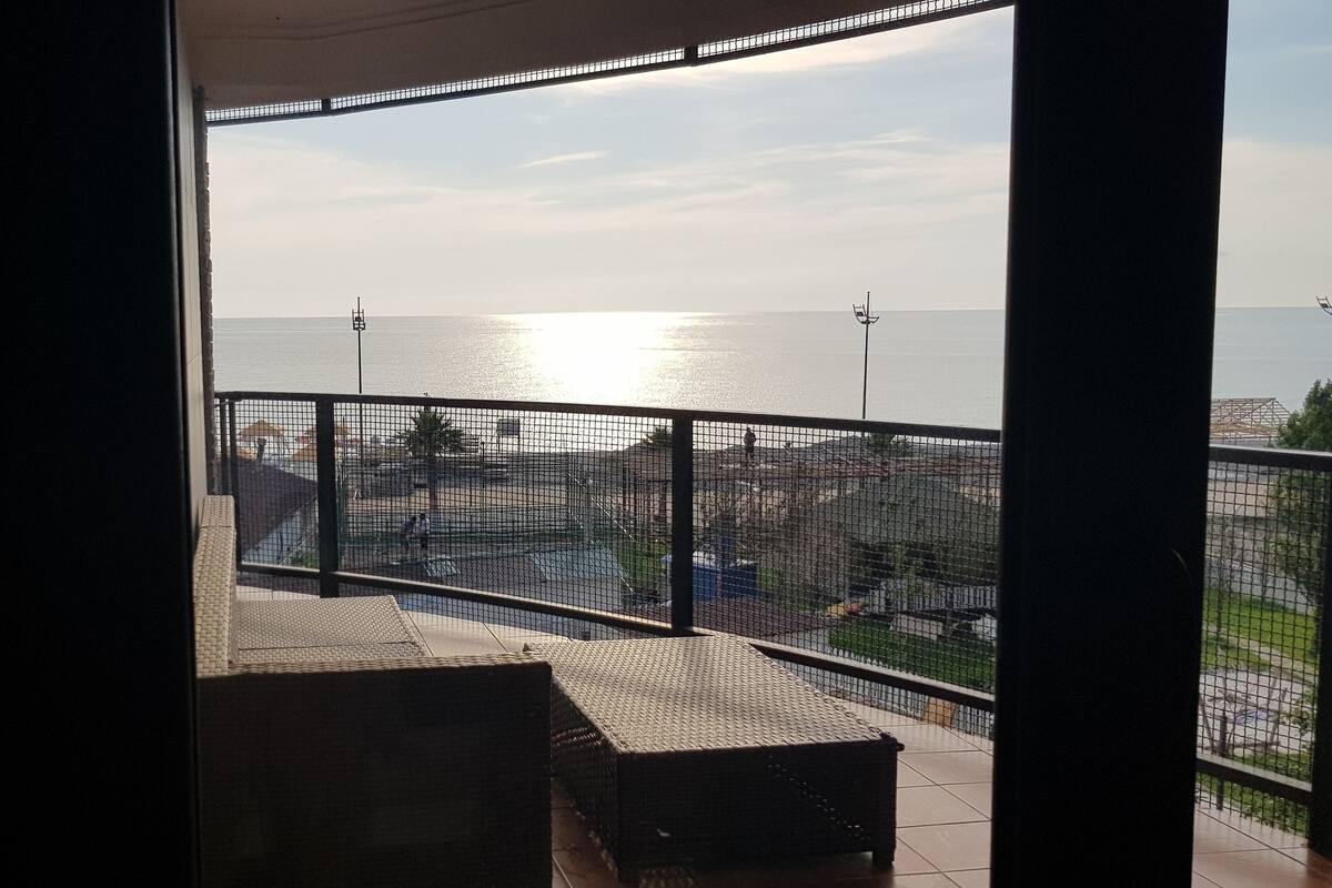 A balcony with a view of the sea and a distant cityscape.