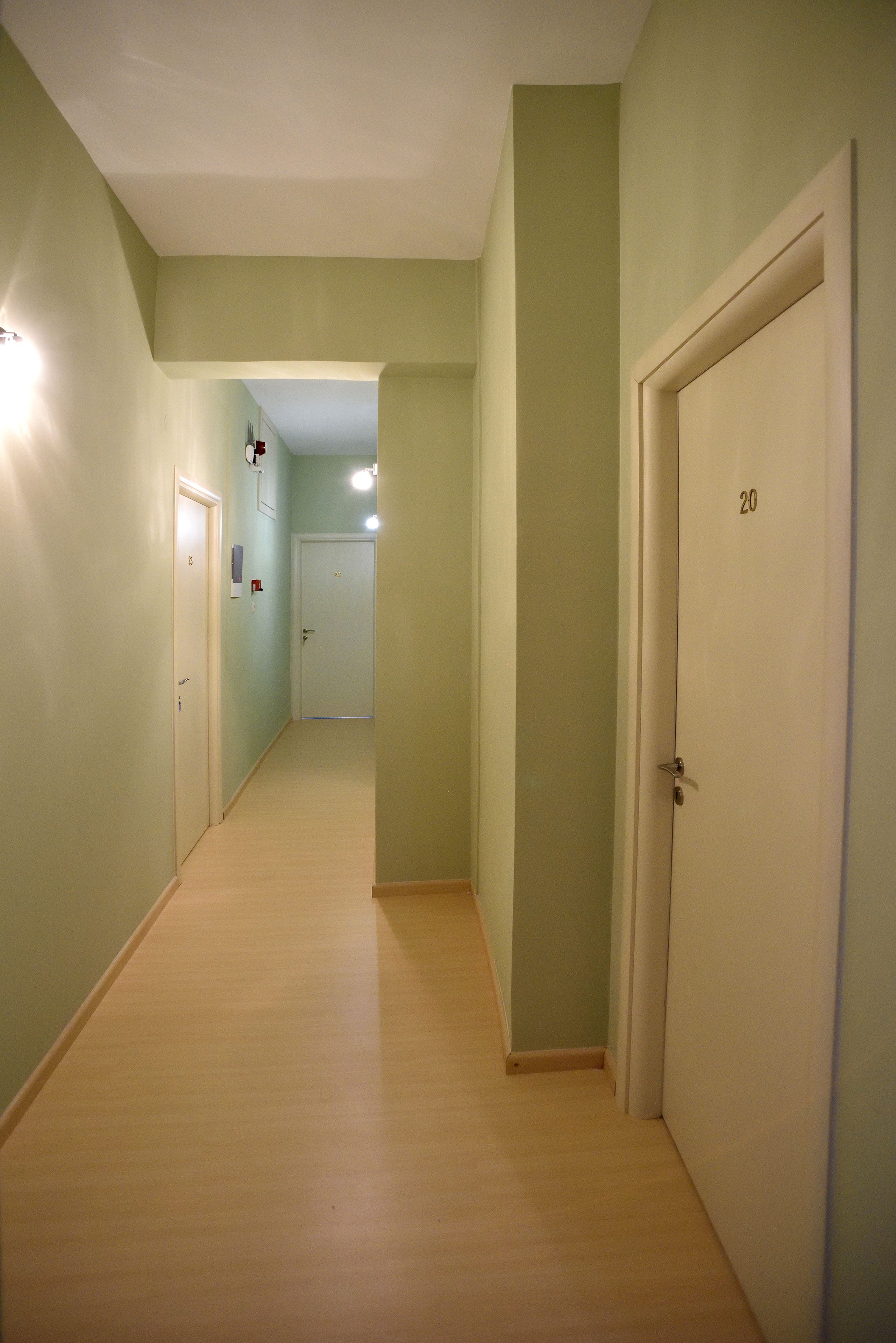 A narrow hallway with light green walls and wooden flooring, leading to a door marked with the number 20.